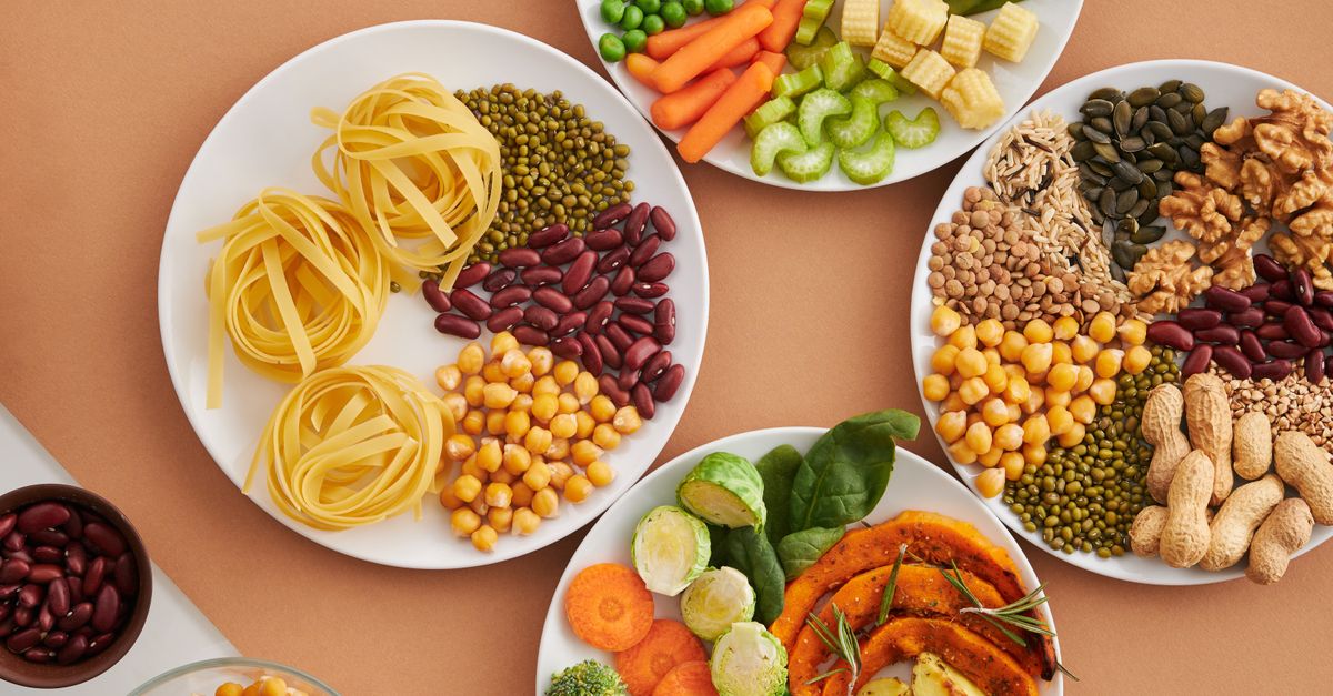 A vibrant mix of legumes, vegetables, nuts, and pasta arranged on white plates showcasing a balanced, healthy diet.
