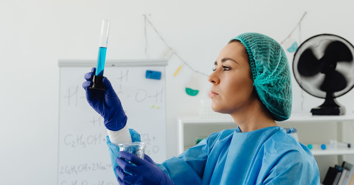Focused female scientist examining blue liquid in test tube at lab.