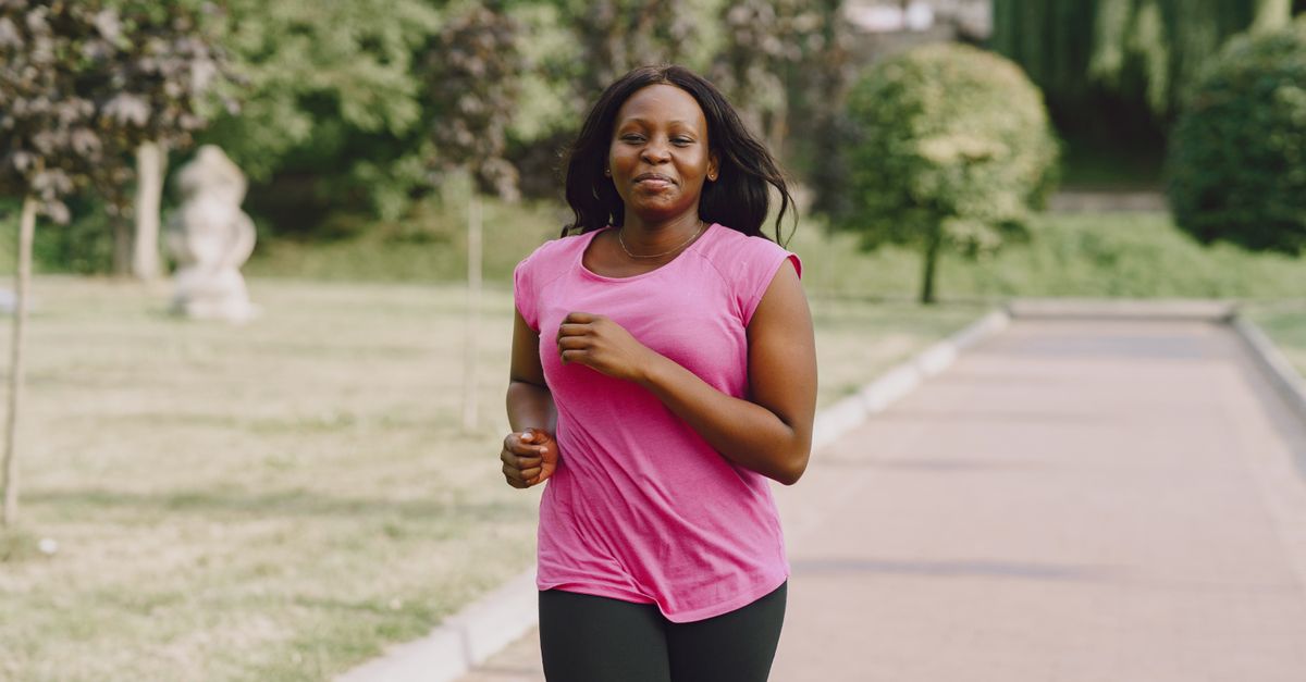 A confident woman jogs along a sunny park path, enjoying a healthy lifestyle.