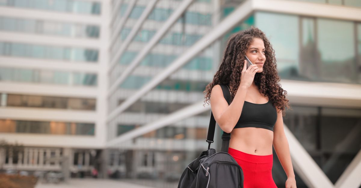 Smiling woman in sports outfit outside a modern building on a phone call.
