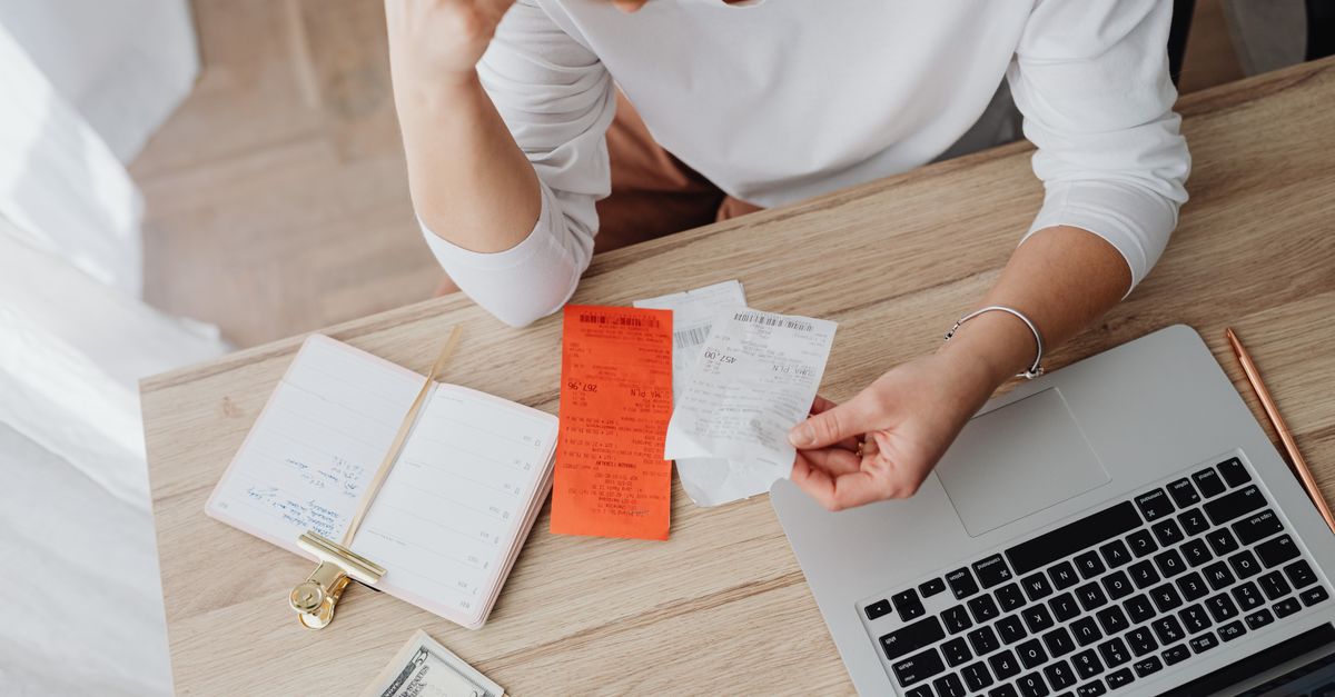 Woman reviewing receipts and planning budget using a laptop and notebook at home to manage expenses.