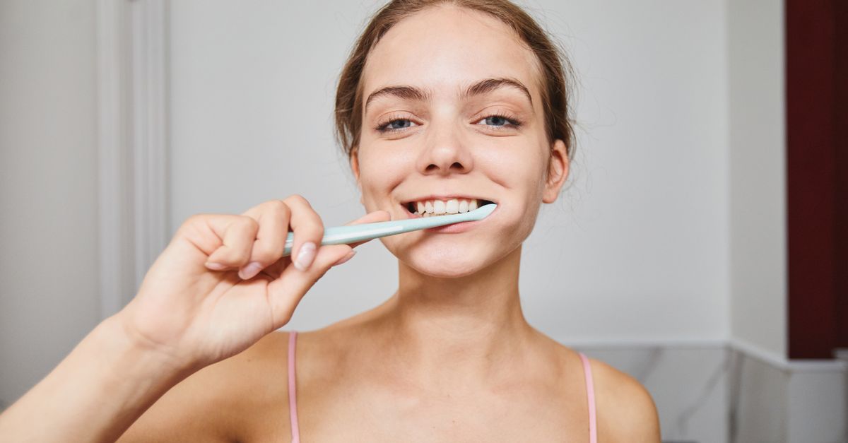 Close-up of a woman smiling while brushing teeth in a modern bathroom.