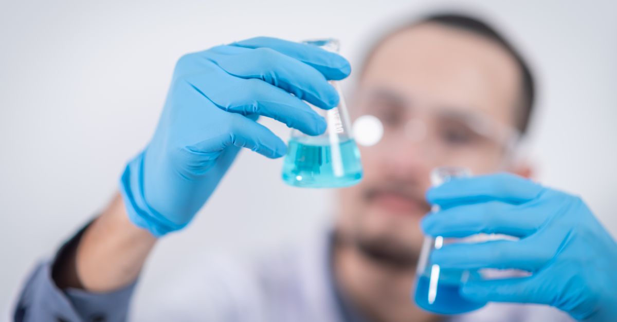Scientist in a laboratory conducting an experiment, holding blue liquid in flasks with protective gloves.