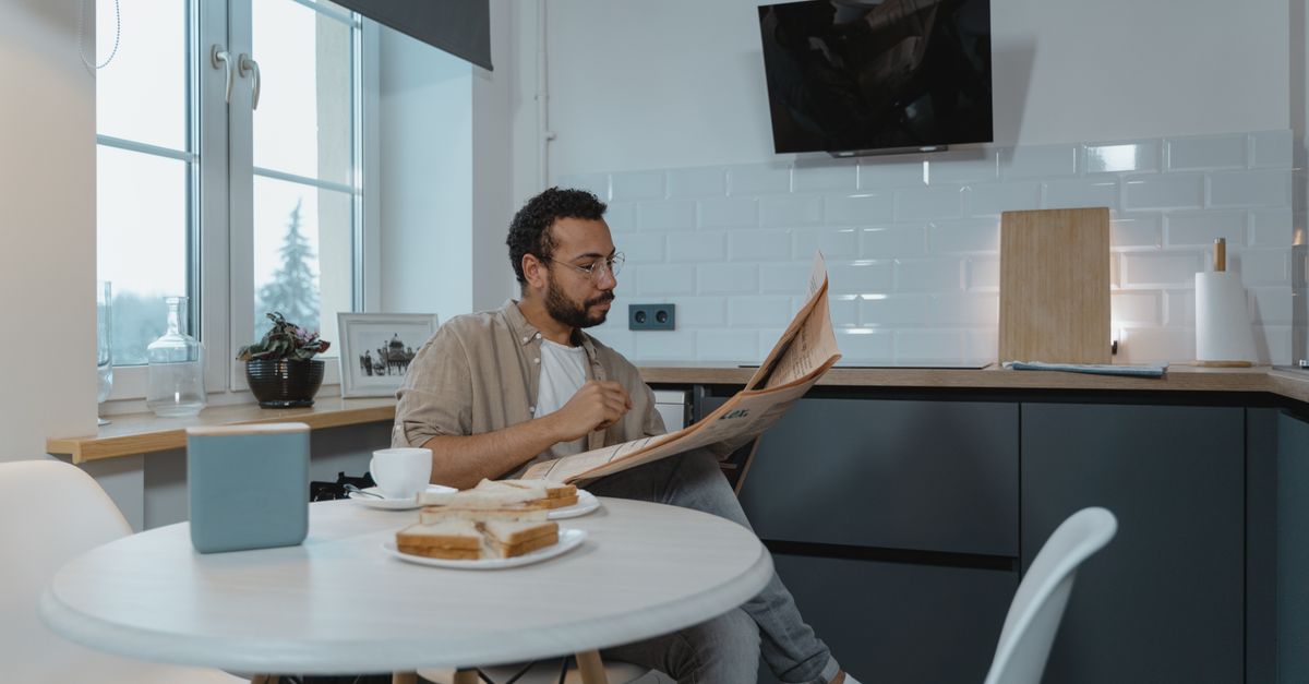 A man reads the newspaper over breakfast in a modern kitchen setting.